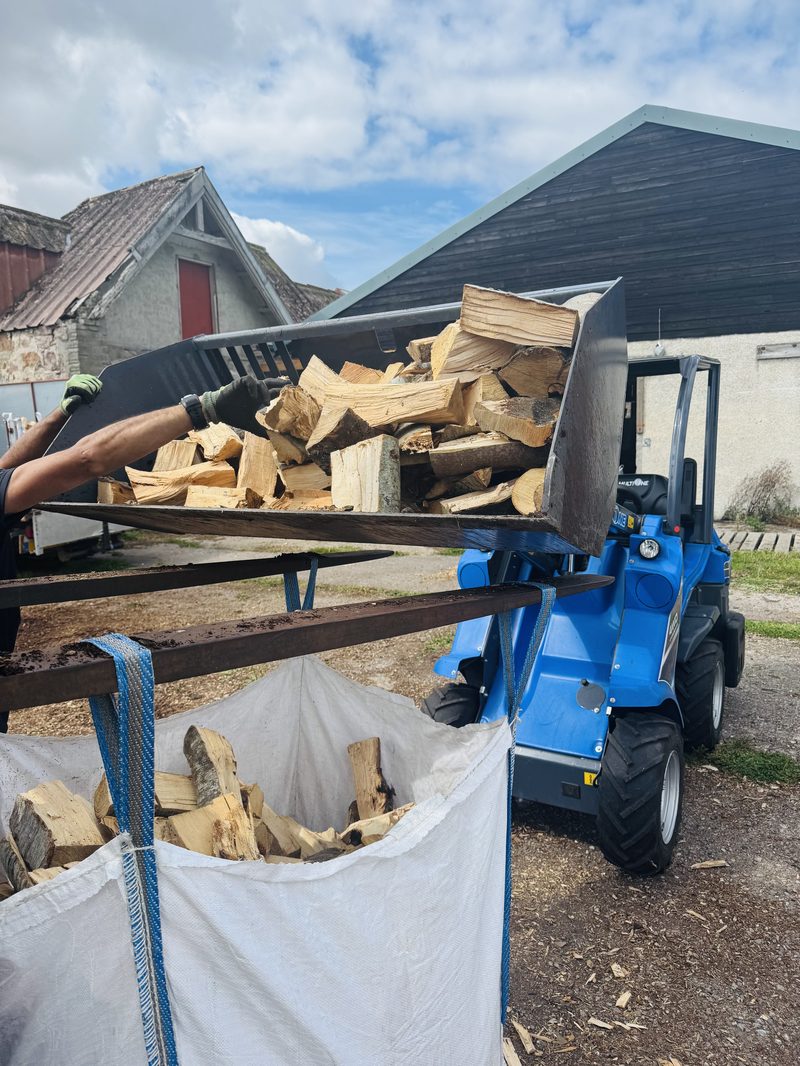 Loader tipping split hardwood logs into a builder's bag